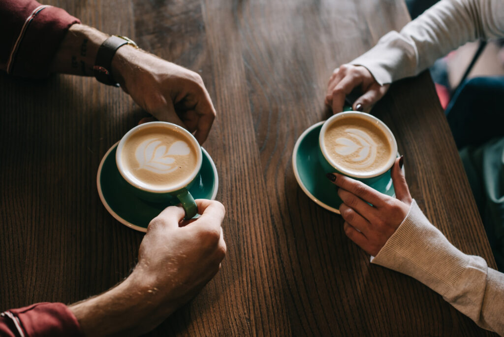 cropped view of couple drinking cappuccino on balcony in coffee shop